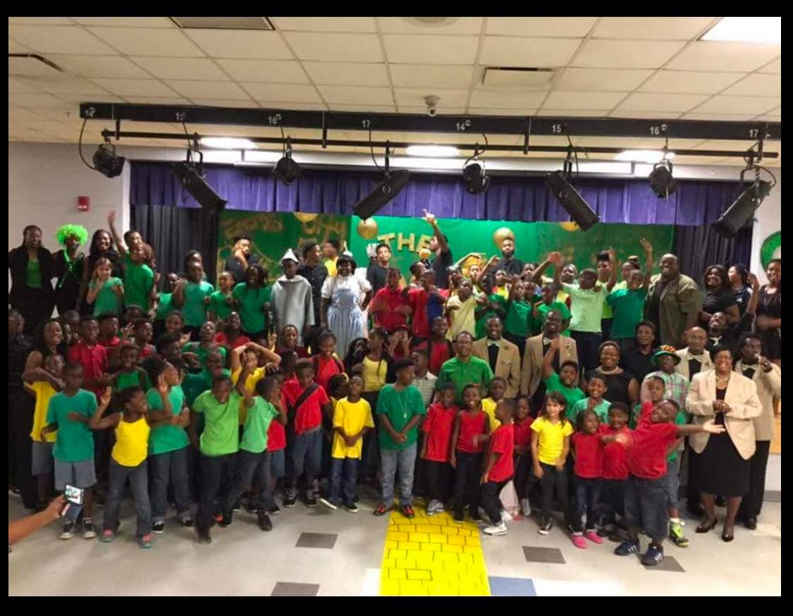 Group of children and adults posing together indoors, wearing colorful shirts.